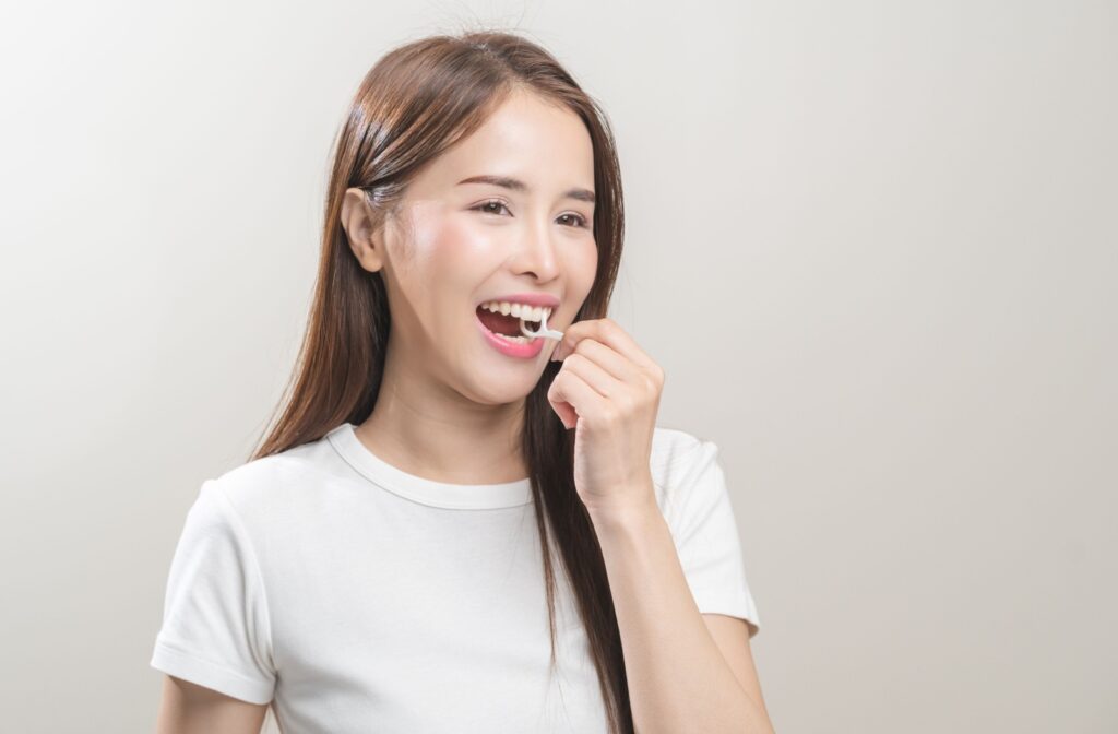 Smiling person using a single-use flosser revealing a white smile against a plain background