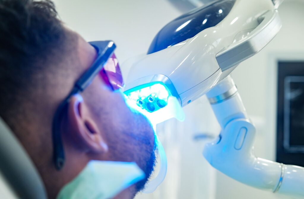 Person receiving teeth whitening treatment with blue curing light at dental office.